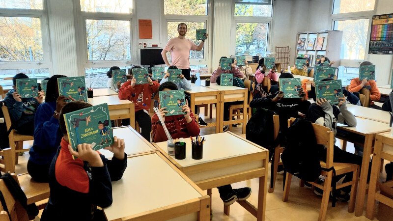 Many pupils sitting and teacher standing in class room holding a book
in front of their face